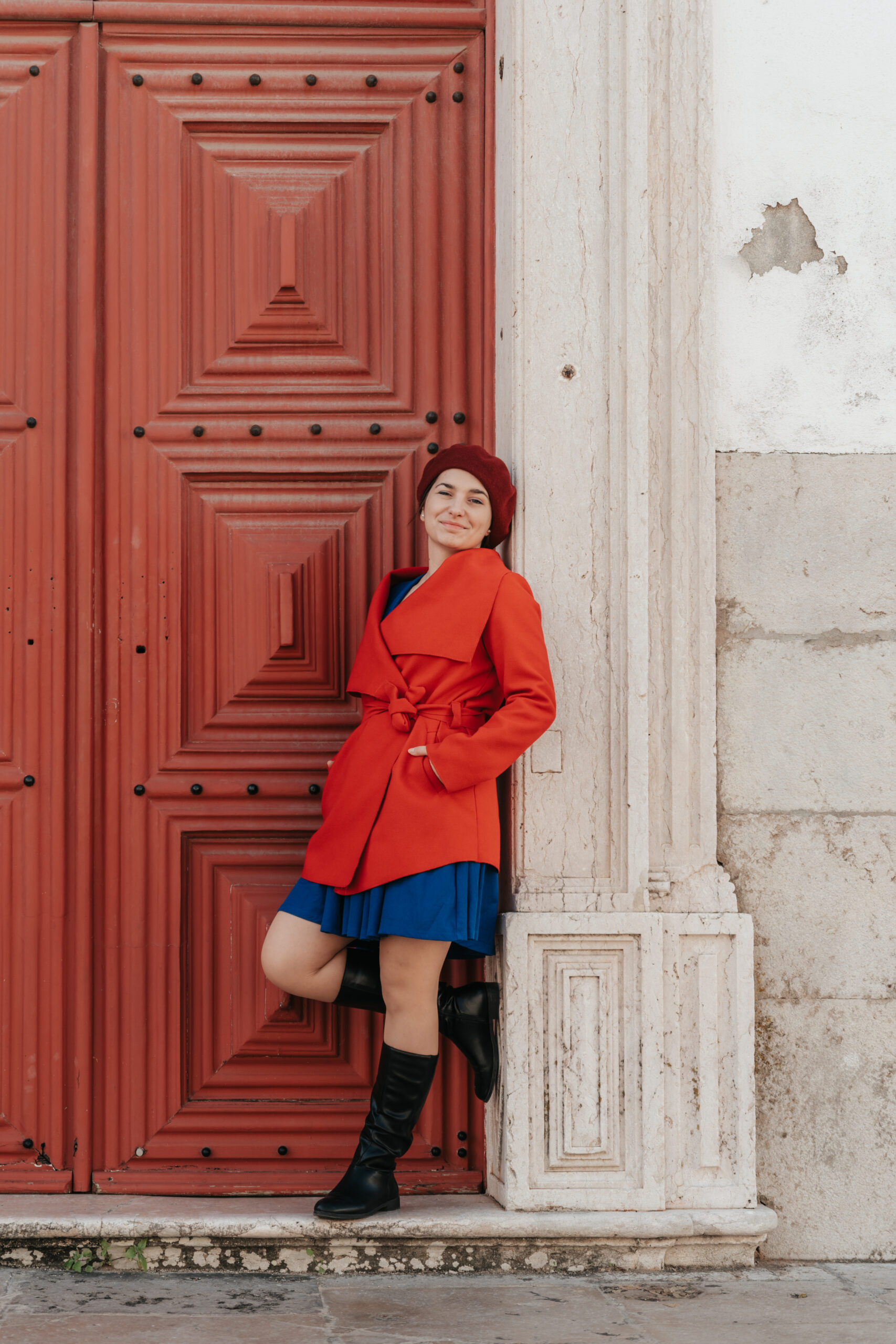 girl standing in front of a red door wearing a red coat